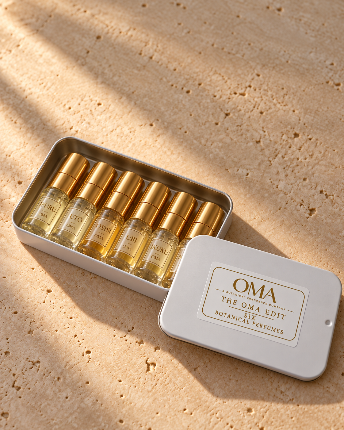 The OMA Edit SIX open white keepsake tin with six labeled perfume vials and gold caps on warm ivory stone; example scent selection