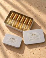 The OMA Edit THREE and SIX discovery sets on ivory stone: closed three-vial tin beside an open six-vial tin with gold caps and labeled lid; example scent selection